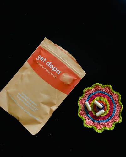 Get Dopa package with colorful crochet coaster featuring small white objects on a black background