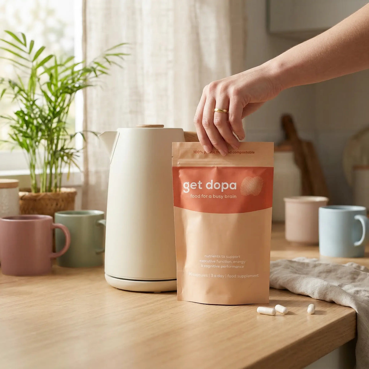 Person holding a 'get dopa' package on a kitchen counter with mugs and a kettle in the background.