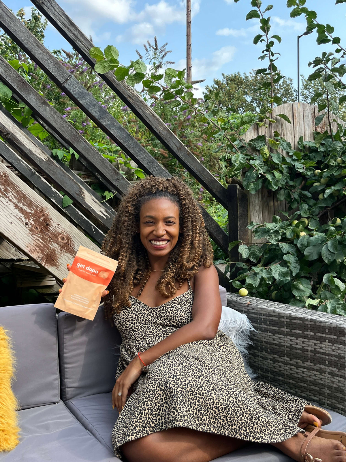 Woman sitting on a couch with 'get dopa, a plant and outdoor furniture in the background